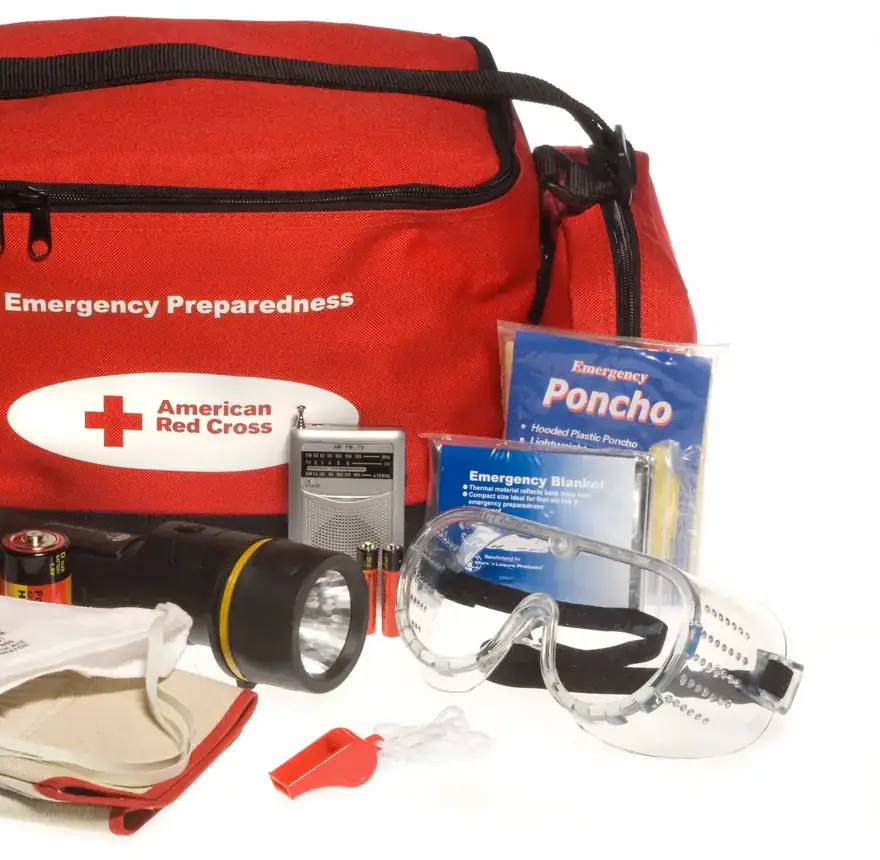 An open Red Cross emergency go bag with water, a radio, a flashlight, and other supplies on a table.