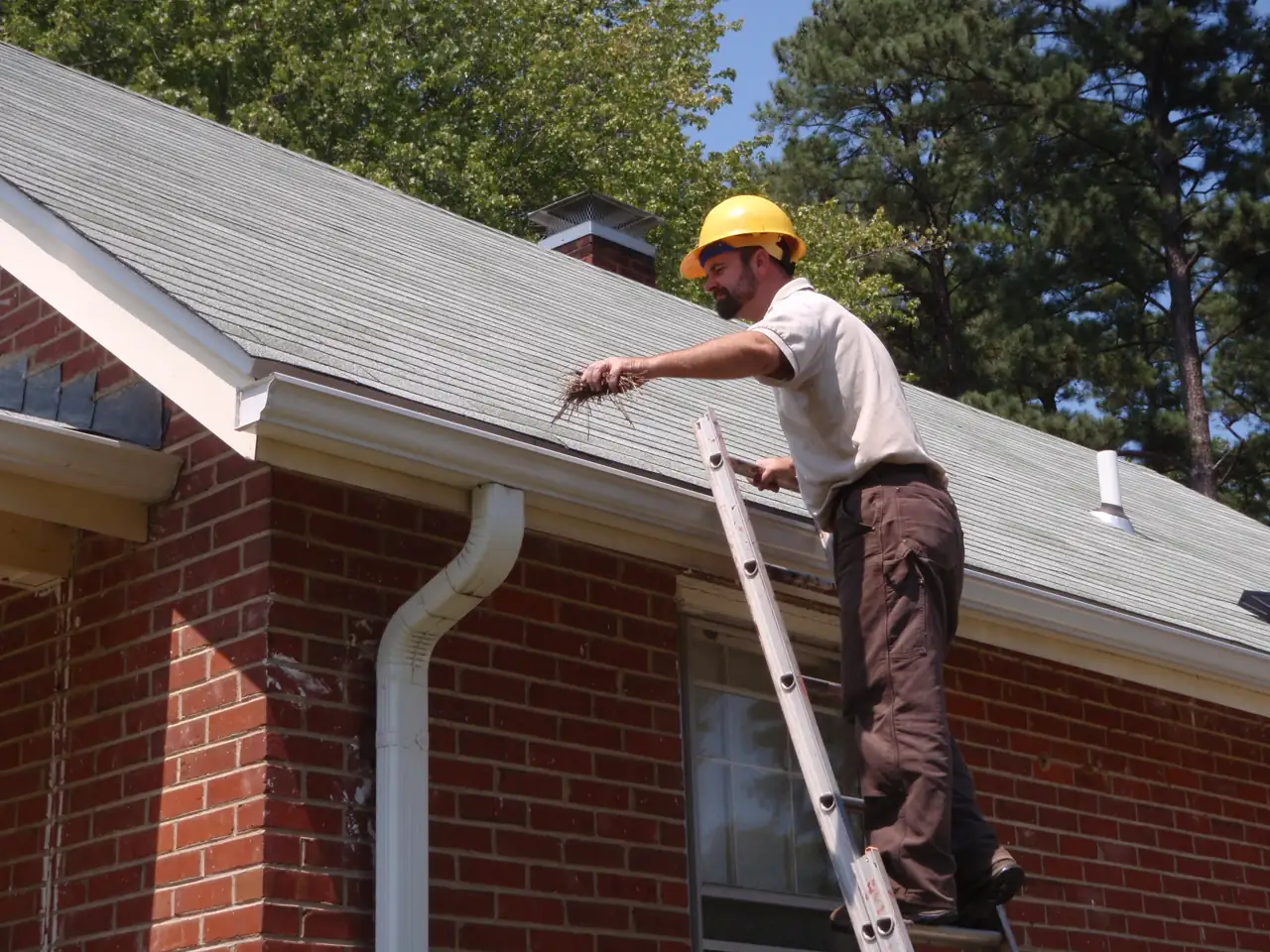 A person on a ladder at the edge of a roof, working at the gutter.
